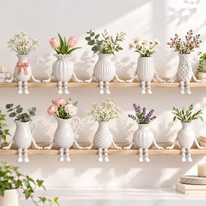 Puede incluir: Una colección de diez jarrones de cerámica blanca, cada uno con forma de pequeña figura con piernas colgantes, sentados en dos estantes de madera. Los jarrones presentan varias texturas y contienen diferentes tipos de flores, como tulipanes y margaritas.