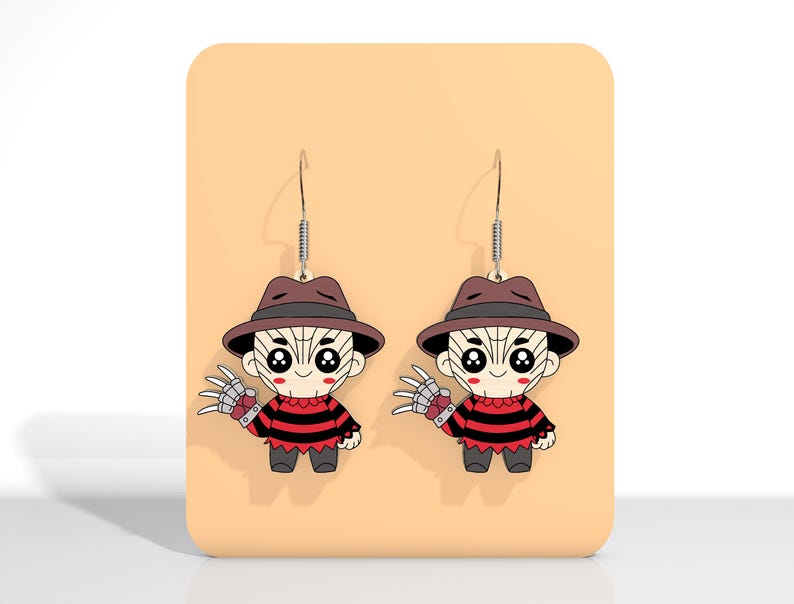 May include: A pair of novelty earrings featuring a cartoon character with a brown hat, red and black striped sweater, and metal clawed glove. The earrings are displayed on a peach-colored card.