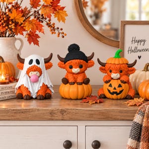 May include: Three orange Highland cow figurines. The first wears a white ghost sheet and blows a pink bubble. The second wears a black knit beanie and sits on a pumpkin. The third wears a pumpkin hat and holds a carved jack-o'-lantern.