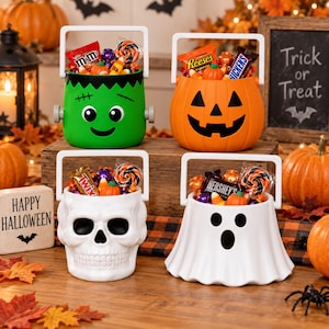 May include: Four plastic Halloween sweet buckets shaped like a green Frankenstein monster, an orange jack-o'-lantern, a white skull, and a white ghost, each featuring a white handle and filled with assorted wrapped sweets and small pumpkin decorations.