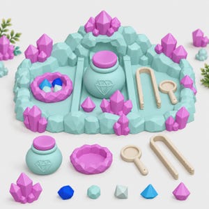 Op de afbeelding: Een lichtblauwe en roze sensorische speelset met kristalthema, bestaande uit een centrale grotstructuur, een pot met deksel en diamanticoon, een kleine kom, beige tangen, een vergrootglas en diverse losse geometrische kristalvormen.