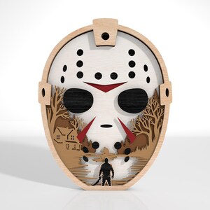 K&ouml;nnte beinhalten: Wandkunst aus Holz mit einem Hockeymasken-Design und einer Landschaftsszene. Die Maske ist wei&szlig; mit schwarzen und roten Akzenten, und die Landschaft umfasst B&auml;ume, ein Haus und eine Figur. Die Kunst besteht aus geschichtetem Holz.