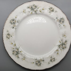 Peut inclure: Assiette plate blanche avec un bord doré et un motif floral de roses blanches et de feuilles vertes.