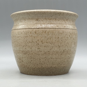 Könnte beinhalten: Ein speckiger beigefarbener Keramiktopf mit runder Form und leicht ausgestelltem Rand.