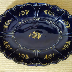 May include: A navy blue oval serving platter with a scalloped edge. The platter features gold floral designs and decorative gold trim. The glossy surface reflects light, highlighting the intricate details of the design. A decorative piece for serving.
