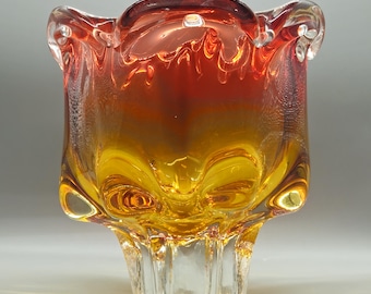 May include: A decorative glass bowl with a unique shape and a gradient of colours. The top is a deep red, transitioning to orange and then to a bright yellow at the base. The bowl has a clear, textured base.