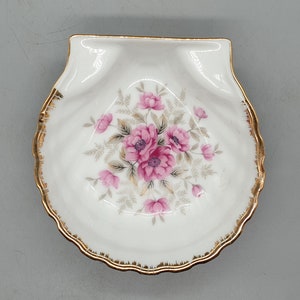 Puede incluir: Un plato de porcelana blanca con un borde dorado y un diseño floral con rosas rosas y hojas verdes.