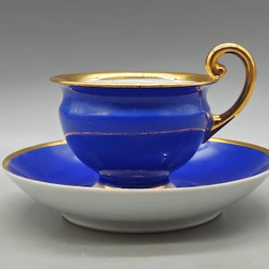 May include: A blue teacup and saucer set with gold trim. The teacup has a curved handle and a gold rim. The saucer is white with a blue center and gold trim. A classic tea set.