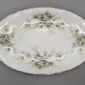 May include: White oval serving dish with a gold rim and a floral design of white roses and green leaves.