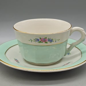 Pode incluir: Um conjunto de chávena e pires de cor verde claro com um desenho floral em rosa, azul e branco. A chávena tem uma borda dourada e o pires tem uma faixa dourada em torno da borda.