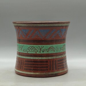 Peut inclure: Un vase en céramique brun avec un motif géométrique en bleu, vert et brun. Le vase a une large ouverture et une base étroite.