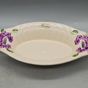 Puede incluir: Plato de servir ovalado de cerámica blanca con diseños florales morados y verdes y las palabras "Rosa Living" en la parte superior.