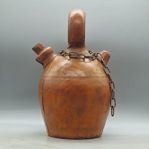 May include: A brown ceramic jug with a metal chain handle. The jug has a cork stopper and a spout.