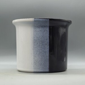 Può includere: Una tazza in ceramica bianca e nera con una striscia blu al centro.