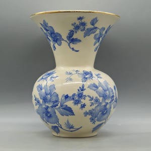 Op de afbeelding: Crèmekleurige keramische vaas met een gouden rand en blauw bloemmotief. De vaas heeft een bolvormige body en een uitlopende bovenkant. Het blauwe bloemendesign bedekt de hele vaas en creëert een klassieke en elegante uitstraling. Een decoratief stuk voor in huis.