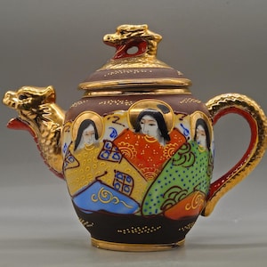 Puede incluir: Una tetera decorativa con cuerpo marrón, detalles dorados y un pico y tapa en forma de dragón. La tetera presenta figuras pintadas con coloridas túnicas. El asa y el borde también son dorados. Una pieza de arte única.