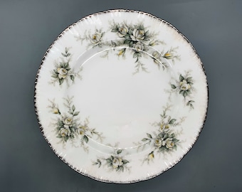 May include: White ceramic dinner plate with a gold rim and a floral design featuring white roses and green leaves.