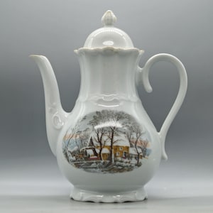 May include: White ceramic coffee pot with a lid and handle. The pot features a winter scene with trees, a church, and a house. The spout and handle have a curved design. The pot is a classic shape and design.