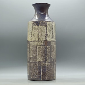 May include: A tall, ceramic vase with a textured, geometric pattern. The vase features a dark brown base, a cream-coloured middle section with rectangular shapes, and a dark blue-purple neck. The vase is approximately 30 cm tall.