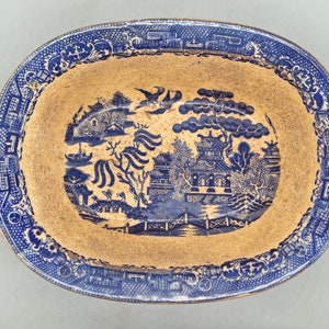 Peut inclure: Un plat ovale en céramique bleu et blanc avec un motif traditionnel de saule pleureur chinois. Le plat est recouvert d'un glaçage doré et décoré d'un saule pleureur bleu, d'un pont et d'une pagode.