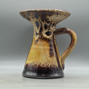Puede incluir: Un jarrón de cerámica marrón y amarillo con una parte superior acampanada y un asa. El jarrón tiene un esmalte moteado.