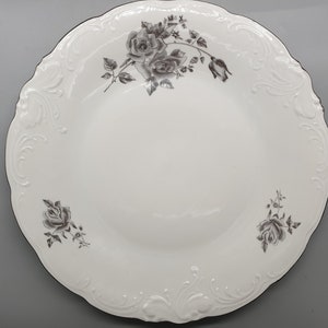 May include: White ceramic dinner plate with a decorative raised rim and a gray floral design featuring roses.