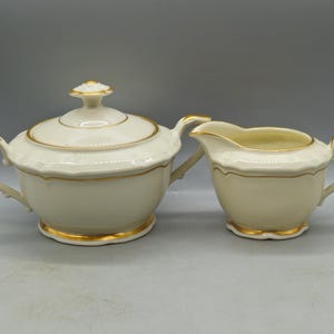 May include: A white porcelain sugar bowl and creamer set with gold trim. The sugar bowl has a lid and both pieces have a scalloped edge.