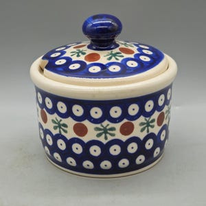 May include: A blue and white ceramic sugar bowl with a lid. The bowl has a floral pattern with red accents.