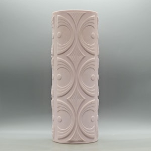May include: A tall, cylindrical vase in a soft, muted pink hue. The vase features a repeating pattern of stylized, symmetrical designs, including circles, ovals, and diamond shapes. The textured surface adds visual interest to this decorative home accent.