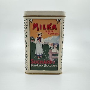May include: A vintage tin box with a white background and green ivy border. The box features a colorful illustration of a girl in a traditional dress holding a stick, with cows and a mountain scene in the background. The text "Milka Letzte Neuheit. Suchard's Voll-Rahm Chocolade." is printed on the box.
