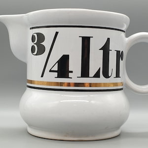 Peut inclure: Pichet en céramique blanche avec une bande noire et dorée autour du milieu. Le pichet a une poignée et indique "3/4 Ltr" en lettres noires.