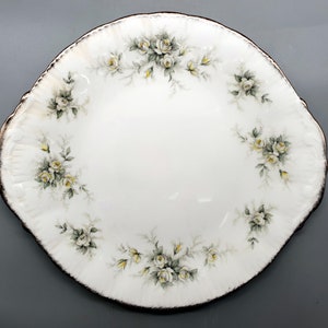 May include: A white oval serving plate with a gold rim and a delicate floral design featuring white roses and green leaves.