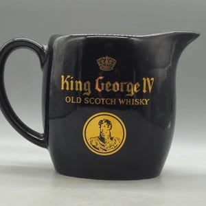 Puede incluir: Jarra de cerámica negra con asa y boquilla. La jarra presenta letras doradas que dicen "King George IV Old Scotch Whisky" y un emblema dorado de un retrato de hombre.