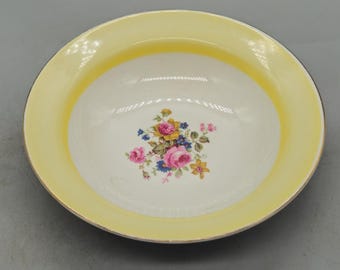 Könnte beinhalten: Eine weiße Keramikschüssel mit gelbem Rand und einem Blumendesign. Die Schüssel hat einen weißen Hintergrund mit einem gelben Rand und einem Blumendesign in der Mitte. Die Blumen sind rosa, gelb und blau.