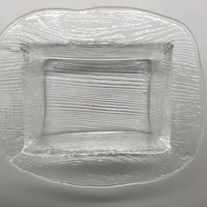 May include: Clear glass serving dish with a rectangular center and a textured, wavy border. The dish is transparent, allowing light to pass through, and is suitable for serving food.