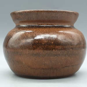 May include: A brown ceramic pot with a rounded body and a slightly flared rim. The pot has a glossy finish and a subtle speckled pattern.