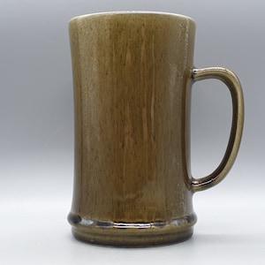 Puede incluir: Una taza de cerámica marrón con una base ancha y un asa redondeada.