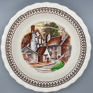 May include: A white ceramic bowl with a brown border and a scene of a village with the text "Blacksmith's Forge".