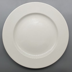 May include: A white ceramic dinner plate with a slightly raised rim.