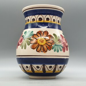 May include: A white ceramic vase with a blue and yellow floral design. The vase has a rounded body and a narrow neck.