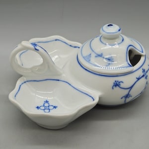 May include: White porcelain serving dish with a blue floral design. The dish has a handle and a separate lidded section with a spoon opening. The design includes a small dish with a floral motif and a scalloped edge.