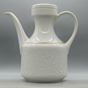 Peut inclure: Une théière en porcelaine blanche dotée d'une base cylindrique avec un motif floral en relief, d'un bec verseur incurvé et fin, d'un couvercle assorti et d'un fin liseré doré entourant la partie centrale au niveau de l'anse.