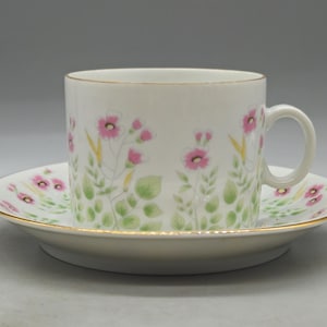 Puede incluir: Juego de taza y platillo blancos con diseño floral. La taza y el platillo están decorados con flores rosas, hojas verdes y tallos amarillos. Los bordes de ambas piezas están adornados con oro. Un juego de té clásico y elegante.