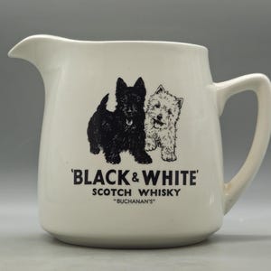 Puede incluir: Una jarra de cerámica blanca con un gráfico negro de un terrier escocés y un terrier blanco de West Highland. Debajo de los perros, el texto dice 'BLACK & WHITE' SCOTCH WHISKY 'BUCHANAN'S' en letras negras. La jarra tiene un asa y un pico vertedor.