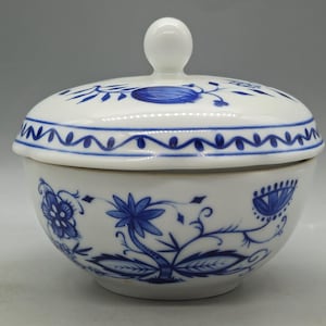 Può includere: Una zuccheriera in porcellana bianca con un motivo floreale blu e bianco. Il coperchio ha un pomo in cima.