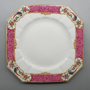 May include: A white octagonal ceramic plate with a pink and gold floral border. The border features a repeating pattern of flowers, leaves, and birds.