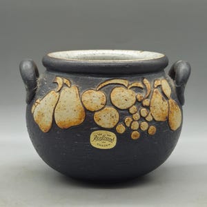 Puede incluir: Una olla de cerámica negra con dos asas y un diseño de frutas blancas y marrones. La olla tiene una etiqueta que dice "Rörstrand Sweden".