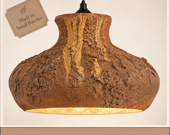 May include: A brown, textured pendant light with a wide, rounded base and a narrow neck, suspended by a black cord. A small rectangular tag attached to the top left reads Made in Small Batches, and a banner at the bottom reads Made to stand out.