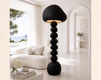 May include: A tall floor lamp featuring a textured black finish with a large, rounded, mushroom-shaped shade atop a vertical stack of seven spherical, textured black orbs that decrease in size toward the top, emitting a warm light from underneath.