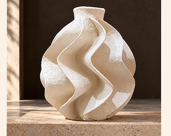 May include: A spherical off-white vase with a textured, matte surface and prominent vertical, wave-like ridges that spiral around the body. The vase features a small, circular opening at the top and a rounded, bulbous shape with a consistent, rough finish.